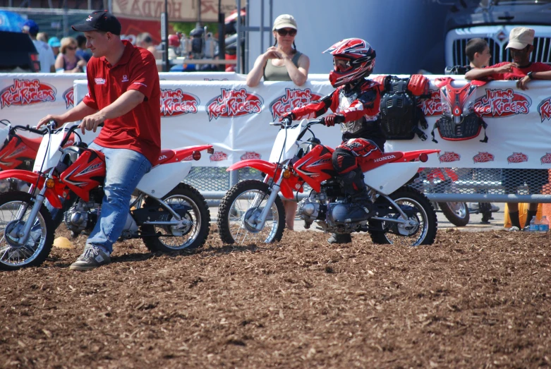 two people are sitting on dirt bikes while others look at them