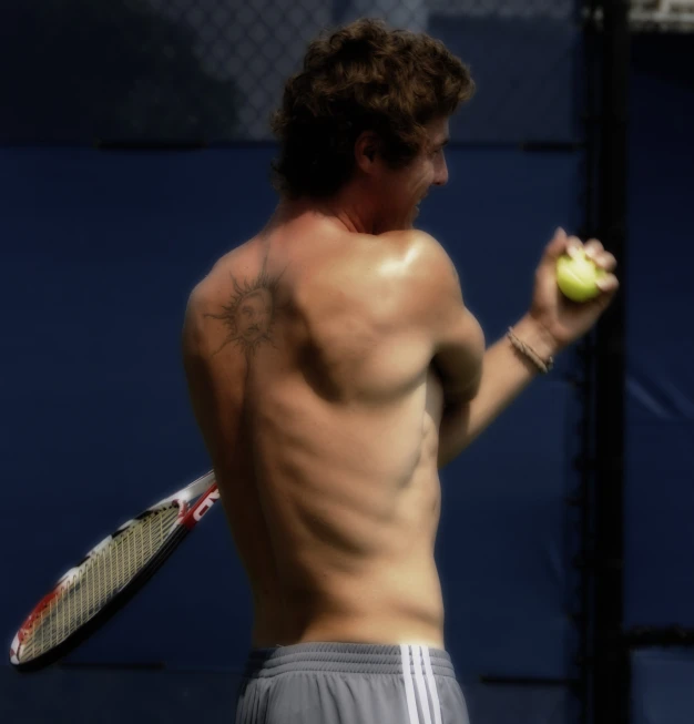 a shirtless man holding a tennis ball and a racquet