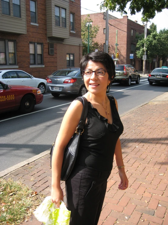 a woman with dark hair and glasses is on the sidewalk