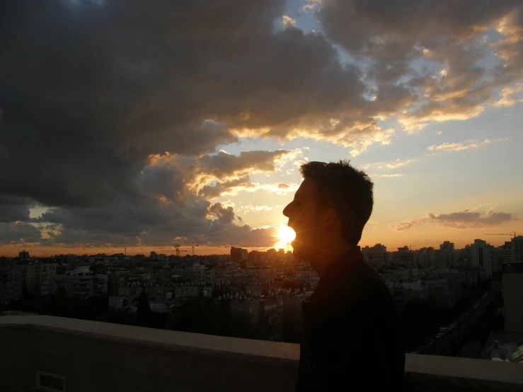 the sun sets behind clouds behind a person standing on a rooftop
