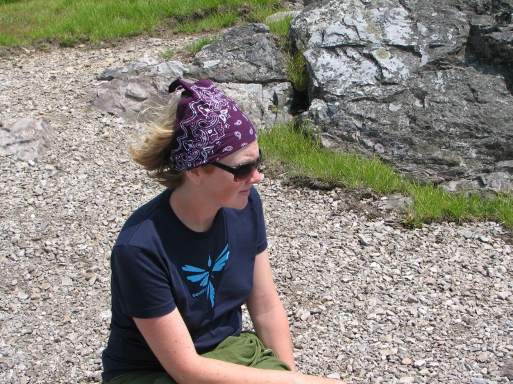 a woman in a blue shirt and purple hat sits on some rocks