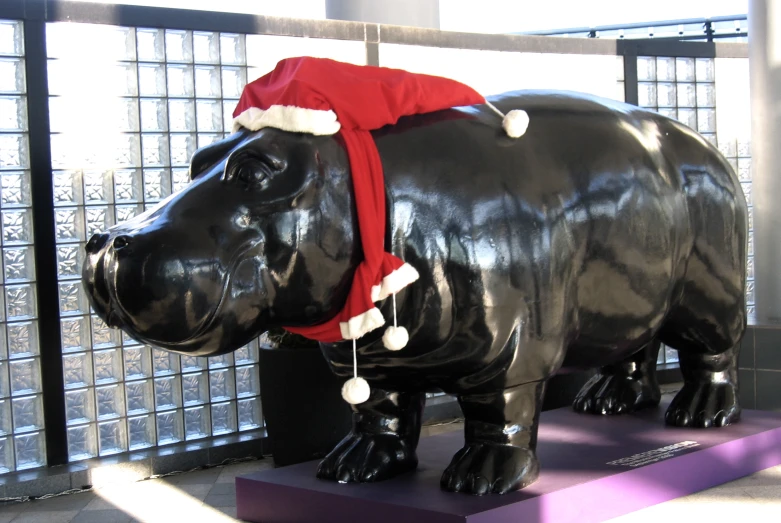 a statue of a hippo with a santa hat on and a scarf tied to its neck