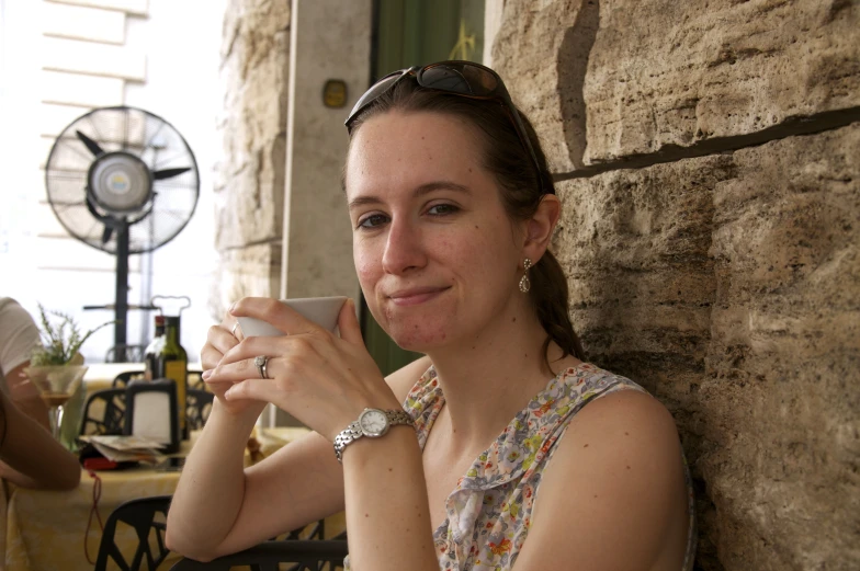 a woman smiles while sitting at a table with a fan behind her