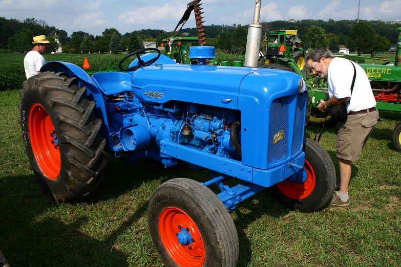 men stand around on the grass with tractors behind them