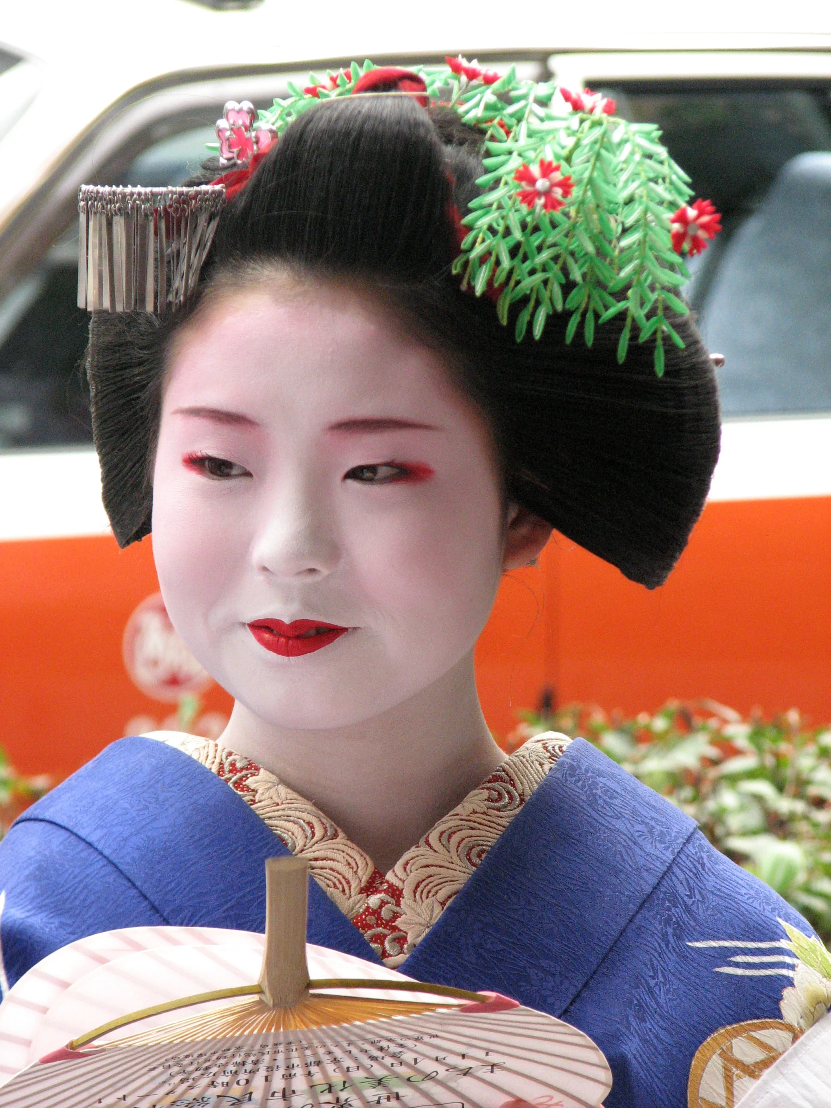 a geisha in a blue kimono with a green plant on her head