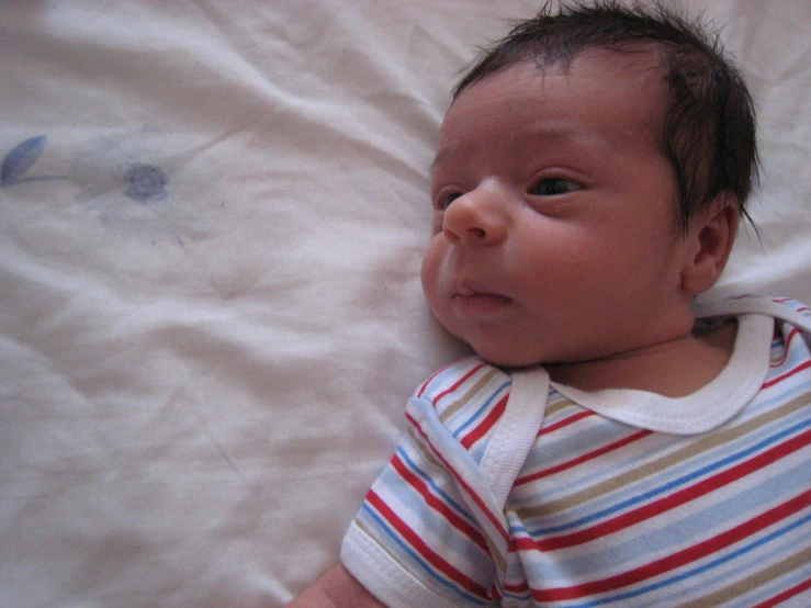 a close up of a baby laying in bed with sheets