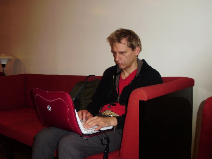 a man sitting on a couch using a red laptop