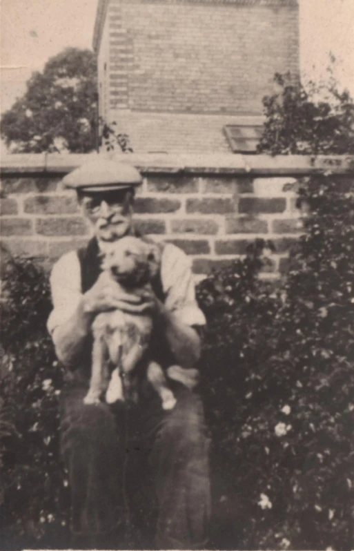 man holding a small puppy while standing next to a brick building