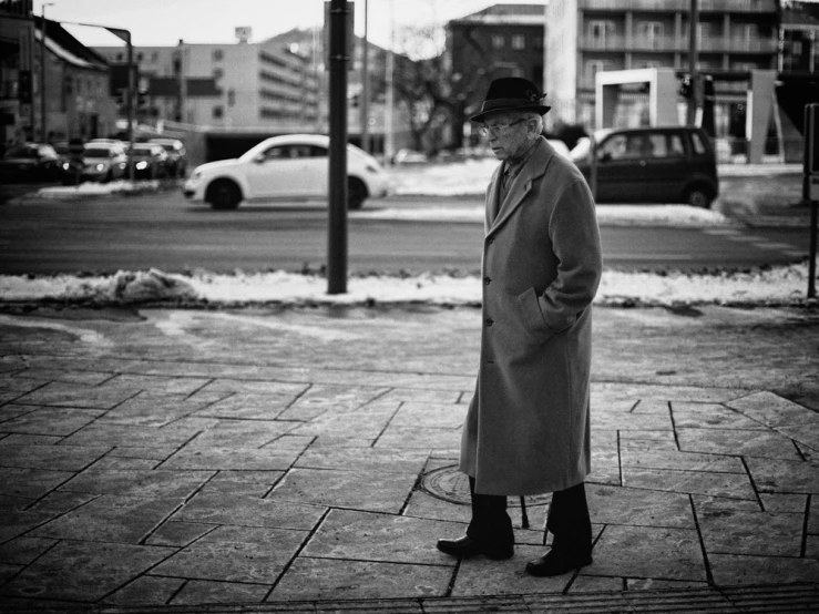 an old man in a coat and a fedora is standing on the street