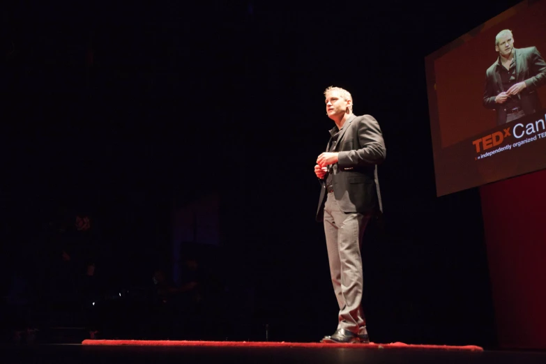 a man standing on stage with a microphone and his hands folded