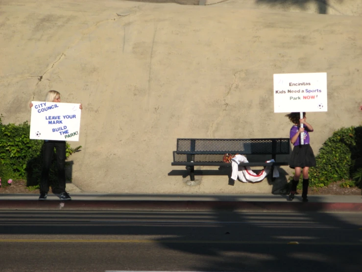 two people holding signs, one of them is laying on a bench