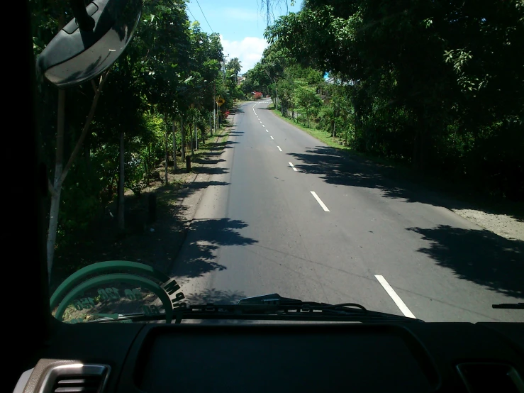 a view from the dashboard of a car of the road through trees and a line of benches