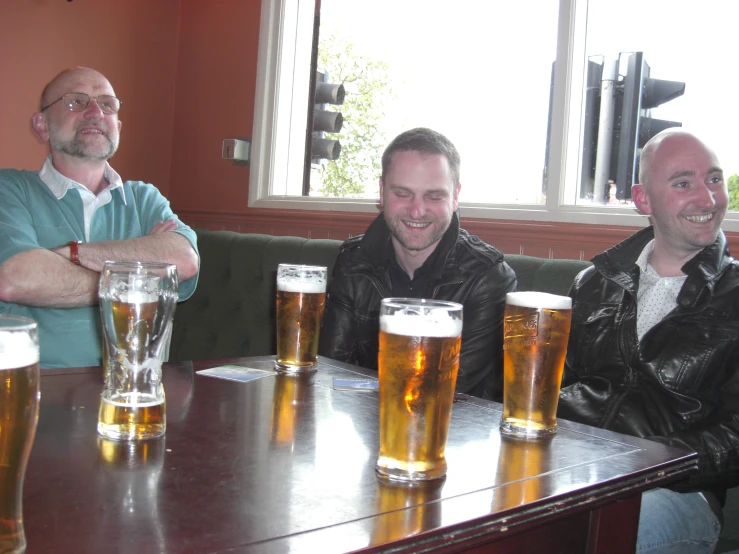 three men are sitting at the table with three beer glasses in front of them