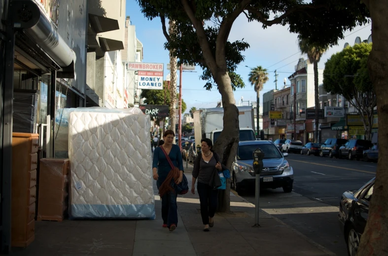 two women walking down a sidewalk next to a mattress