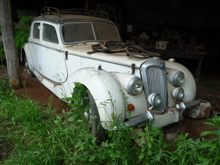 an old white car is outside in the dirt