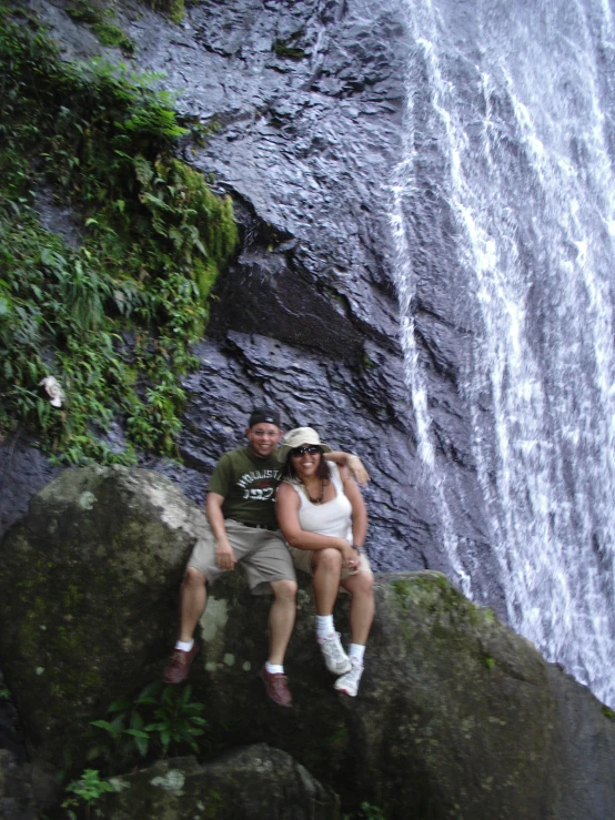 a man and a woman sitting on top of rocks near a waterfall