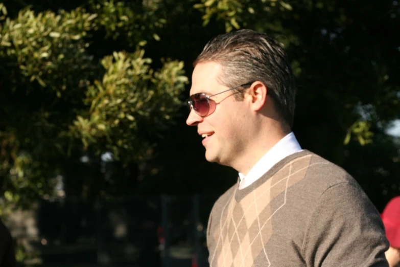 a man wearing a sweater and sunglasses is standing under a tree
