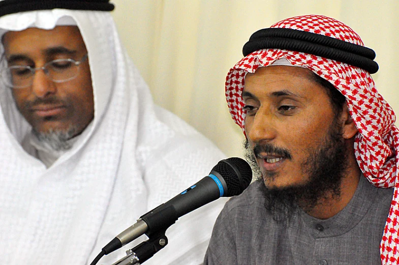 two men wearing head coverings on stage and microphones