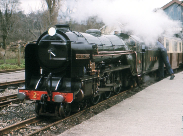 the man is standing on the platform beside a steam train