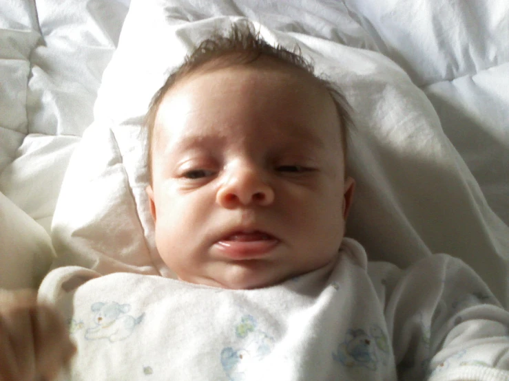 baby being snuggled in white blanket next to white sheets