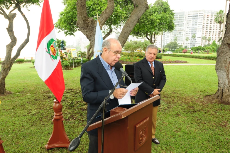 two men are speaking while standing near flags