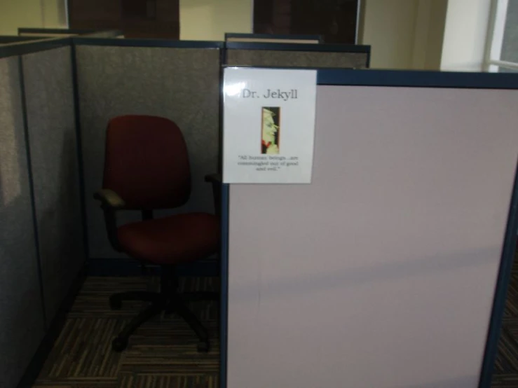 an office cubicle with a pink wall and grey paneled walls with a sign on it