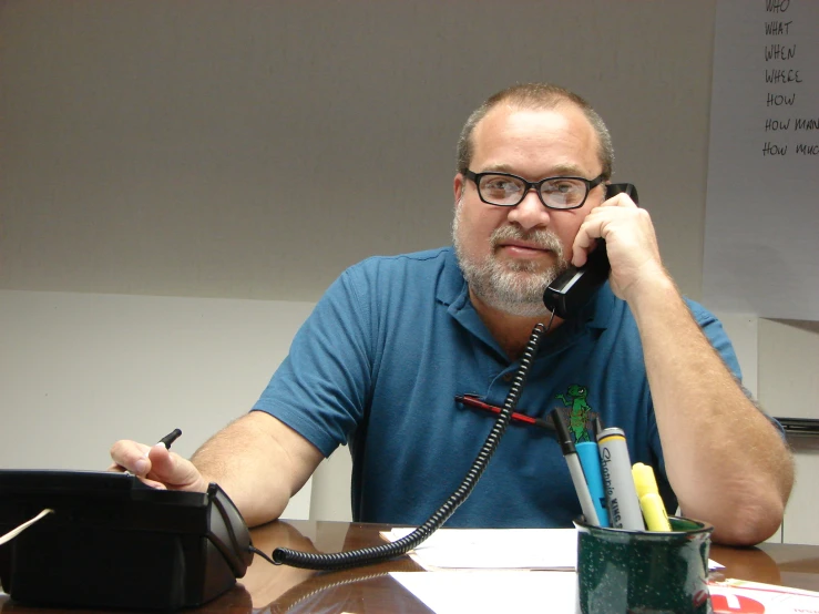 a man in blue shirt on telephone next to desk