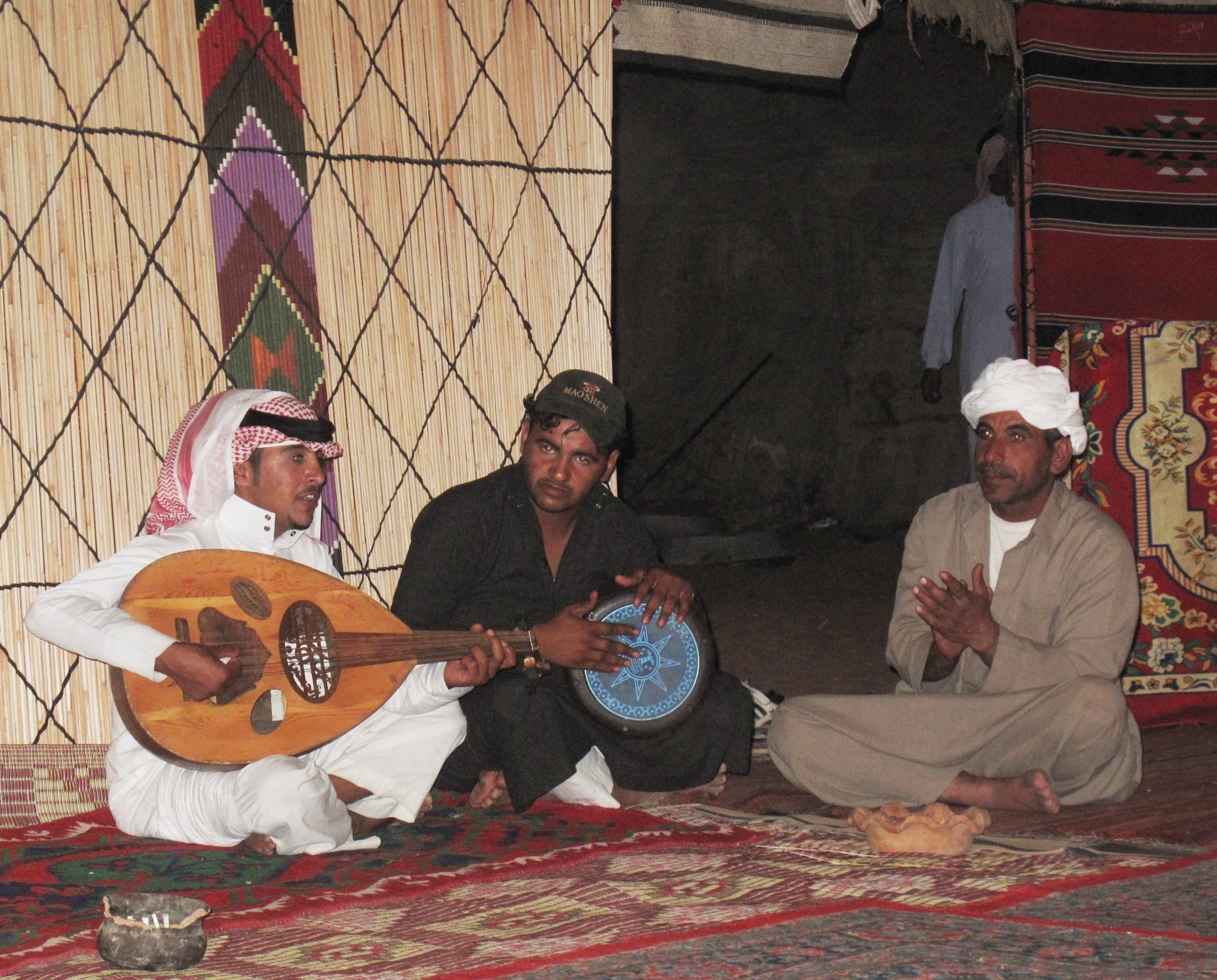 two men sit and play their guitars while others look on