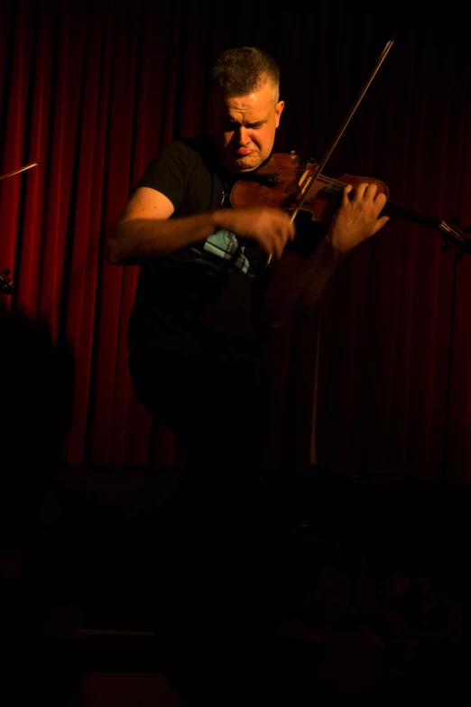 a man holding onto a violin in front of a red curtain