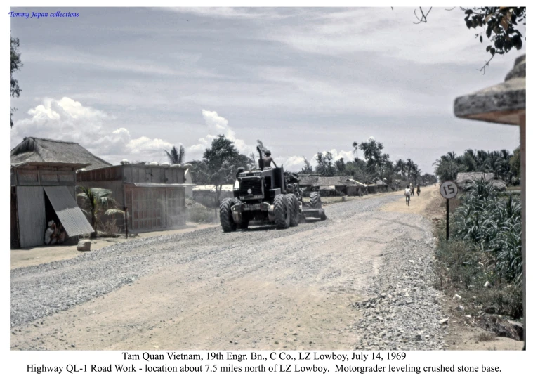 an army vehicle driving down a road near a building