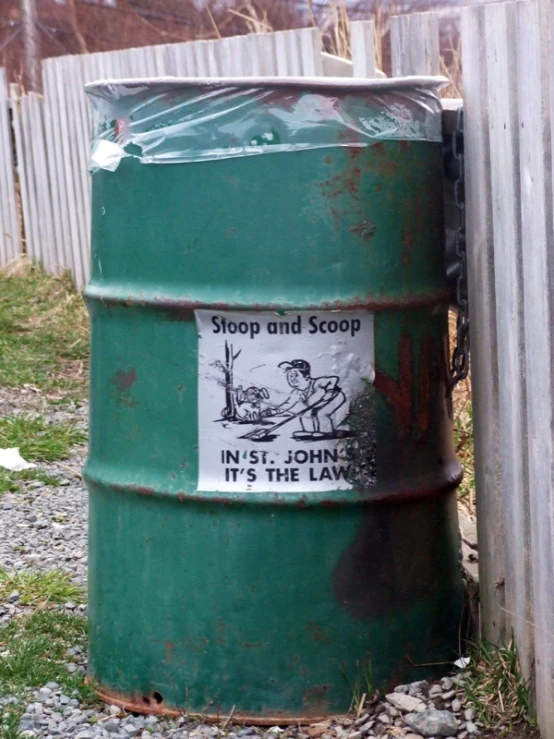 a green barrel on the ground behind a metal fence