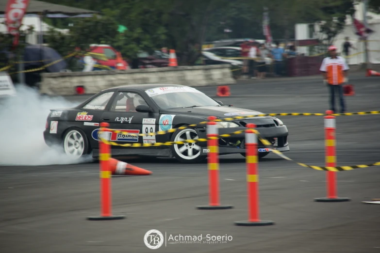 a small car drifts past orange and yellow barriers