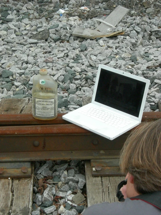 a laptop is on a railroad track next to a bottle of whiskey