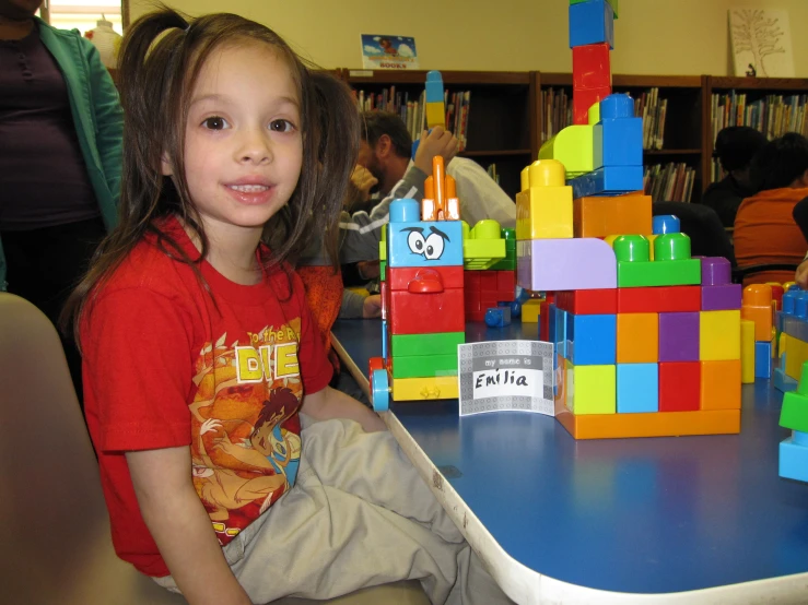 a little girl sitting at a table with lots of colored blocks on it