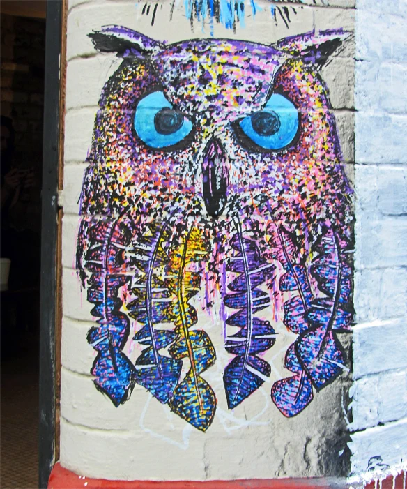 graffiti on a brick building depicting an owl with bright blue eyes and a pink feather