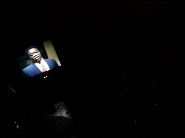 a dark background with television showing a man in a suit and tie