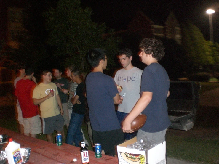 several young men stand at a table outside at night