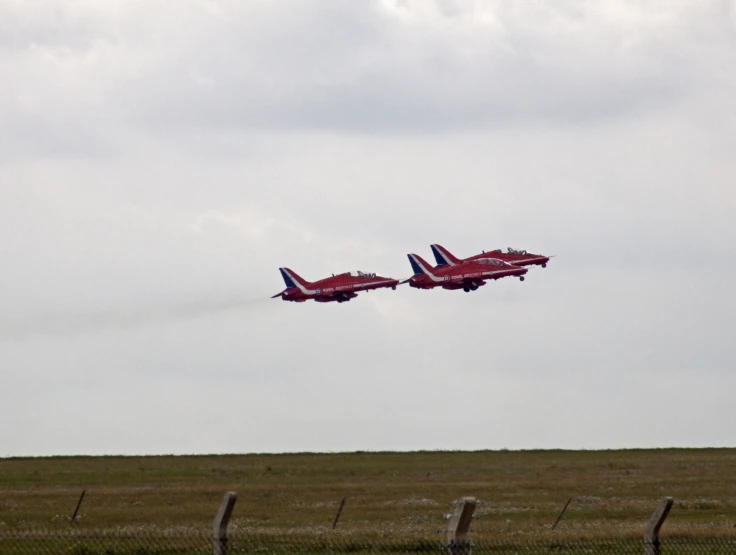 two red and black jets fly in formation over the grass