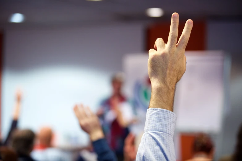 people in an auditorium raising their hands up for the camera