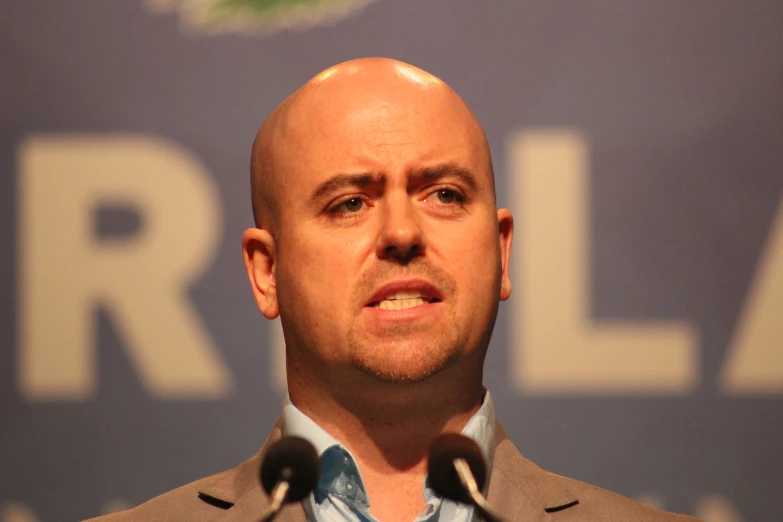 a bald man is speaking at a press conference
