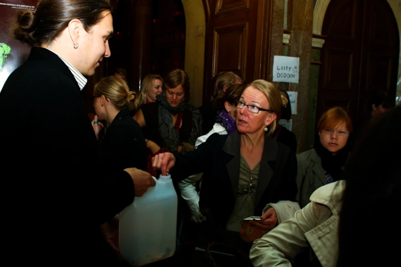 a man with eye glasses is speaking to someone in a crowd