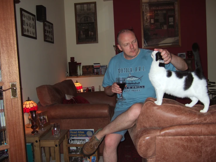 a man holding a glass with his cat sitting on the couch