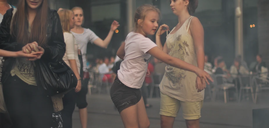 two girls stand on a sidewalk with their hand in the air