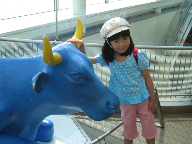 a little girl standing next to a statue of a blue bull