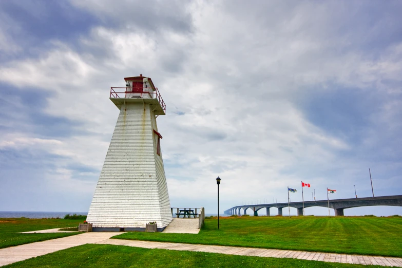 a light house stands at the end of a walkway on a grassy hill