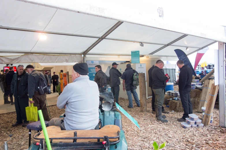 men stand under umbrellas in an outdoor area, with people sitting and standing around