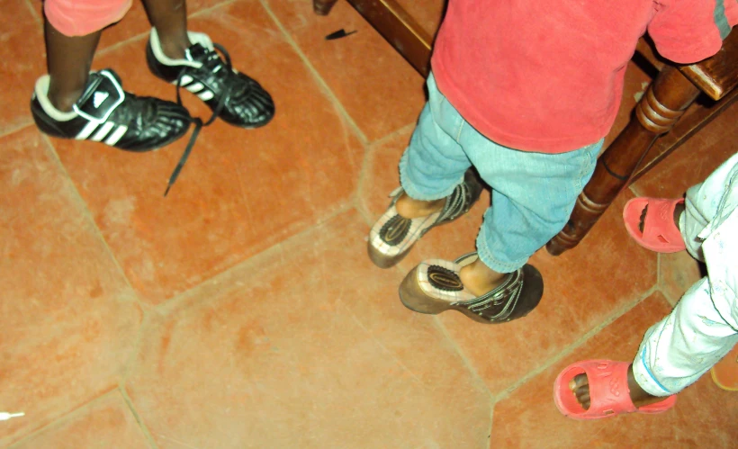 several small children standing on the ground, shoes up close