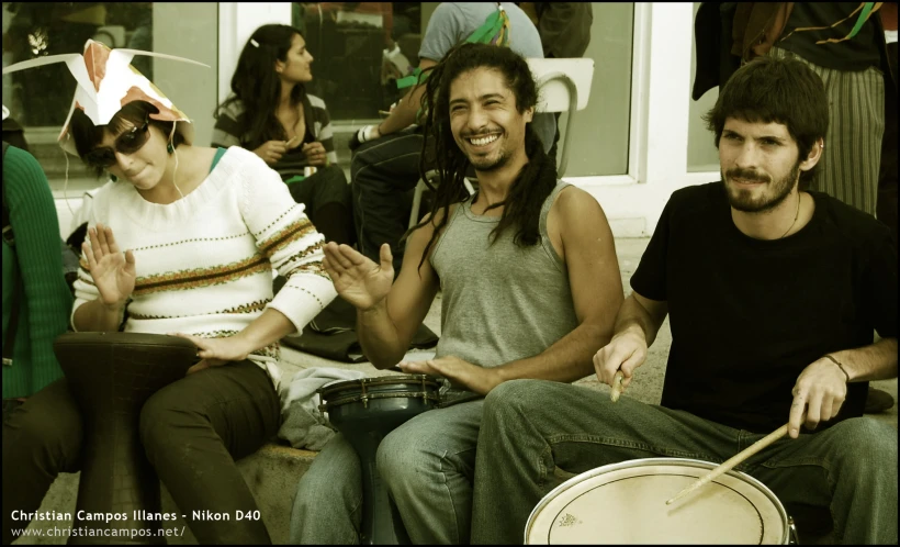 a group of friends sit on a bench, one holding a instrument and clapping