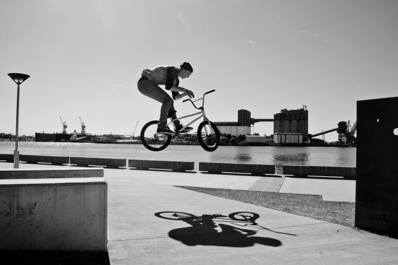 black and white image of man jumping on bicycle over water