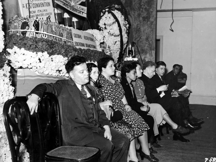 a group of people sitting in chairs, next to a flower clock